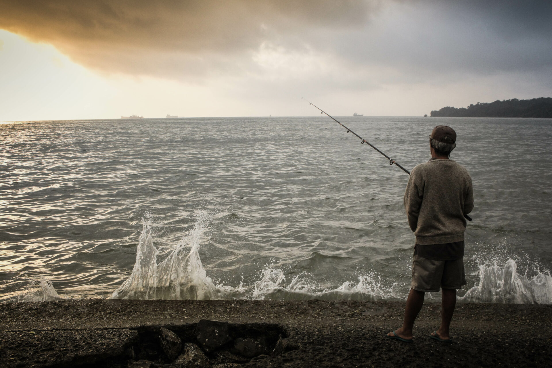 ,am standing and surf fishing from shore with cloudy sky in front of him